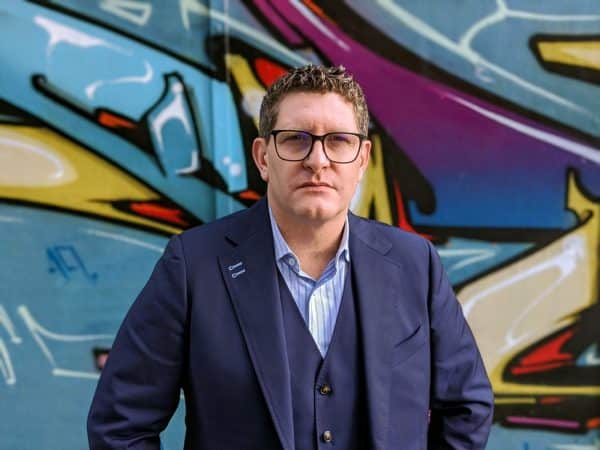 Jason Partridge Lux Research Vice President of Client Experience wearing a navy suit in front of a graffiti wall.