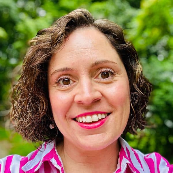 Headshot of woman with shot brown curly hair, pink lipstick, and pink and white striped shirt.